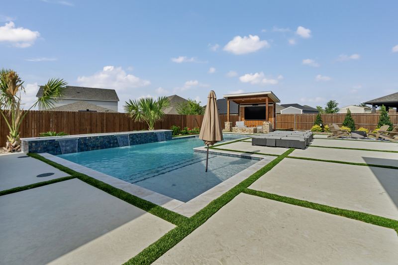 Concrete deck with turf strips and coping beside a tiled pool